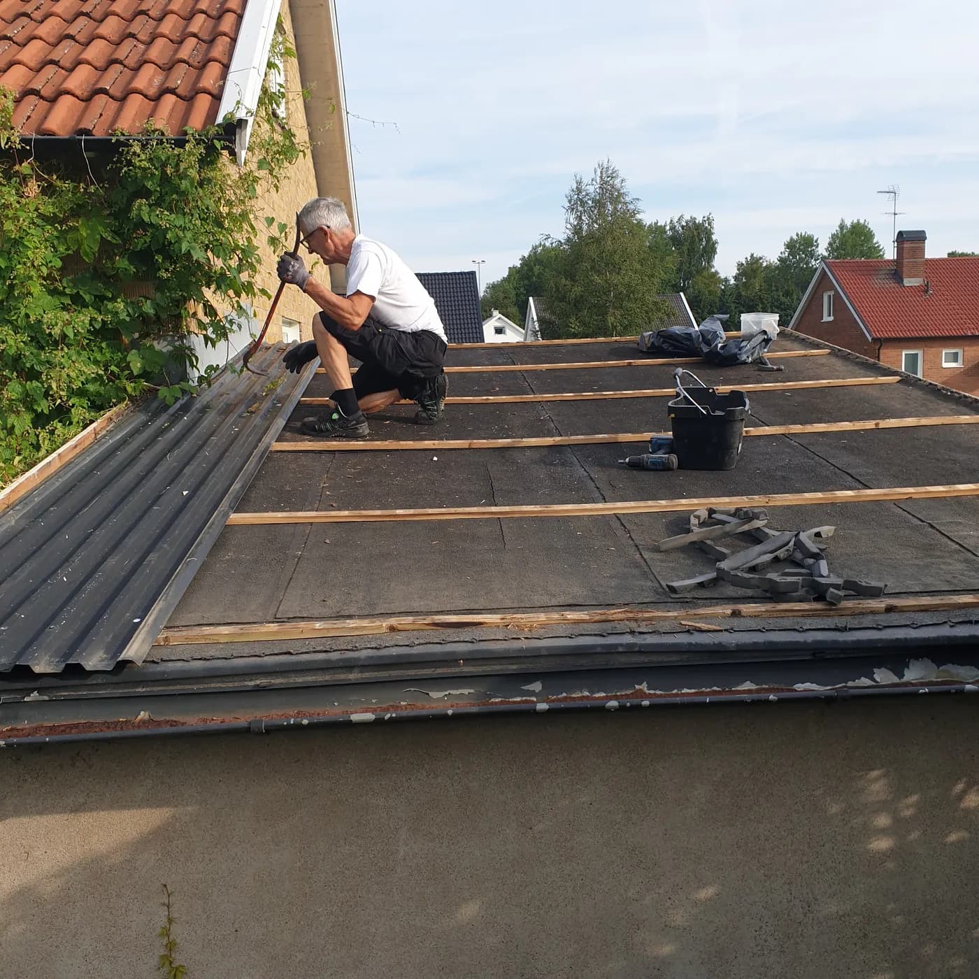 Takläggare bänder loss de sista plåtprofilerna från garagetaket med kofot.