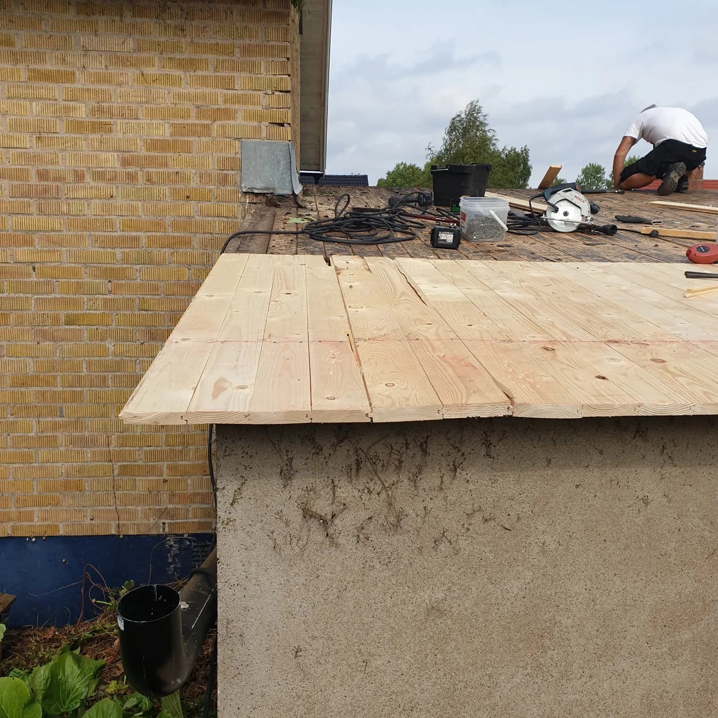 Ny råspont läggs planka för planka över garagetaket, ljust virke mot det gamla underlaget.