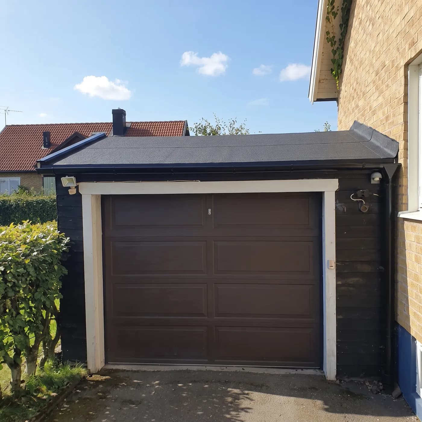 Garaget sett framifrån från infarten med färdigt papptak, ny hängränna och nytt stuprör.