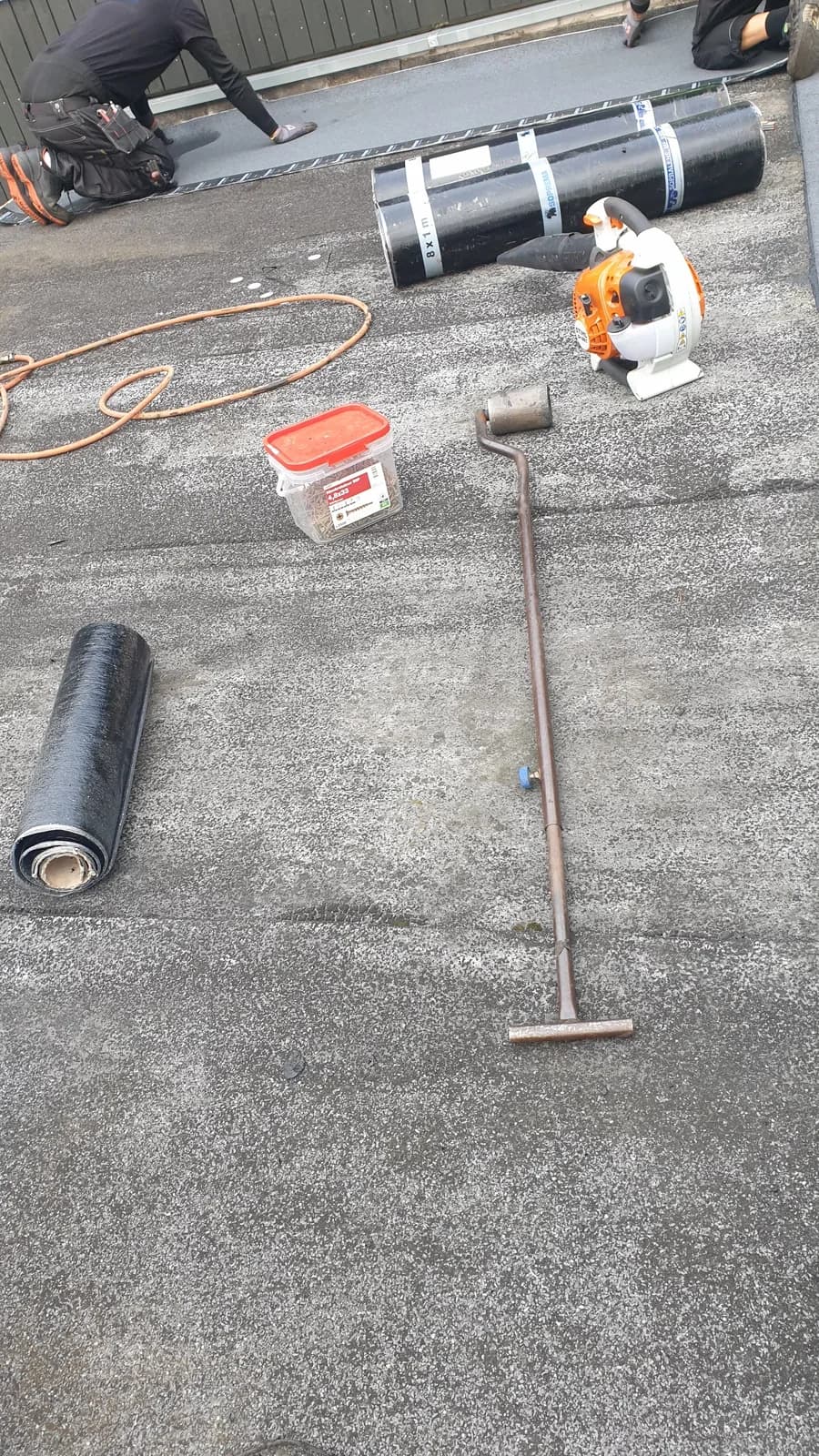 Den gamla pappen på garagetaket i Mölndal, grå och fläckig, med nya pappruller och verktyg framlagda.