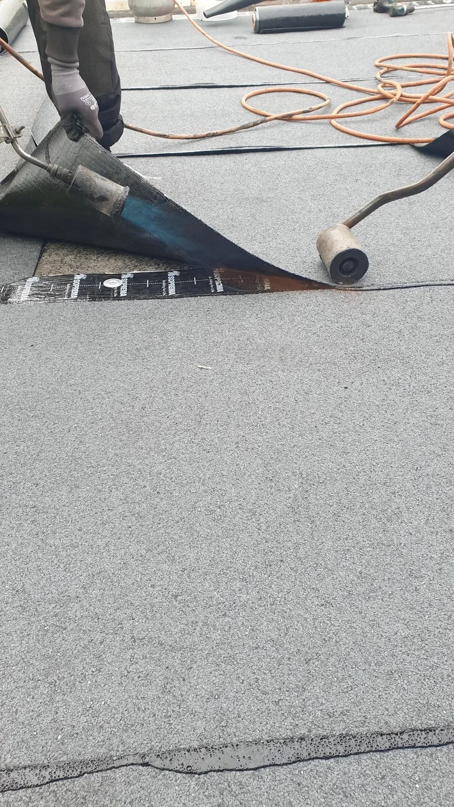 Smält asfalt pressas ut i skarven när valsen rullar efter brännaren.